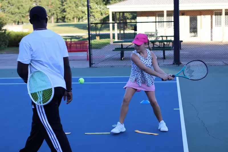 Junior player hitting a backhand while her coach watches